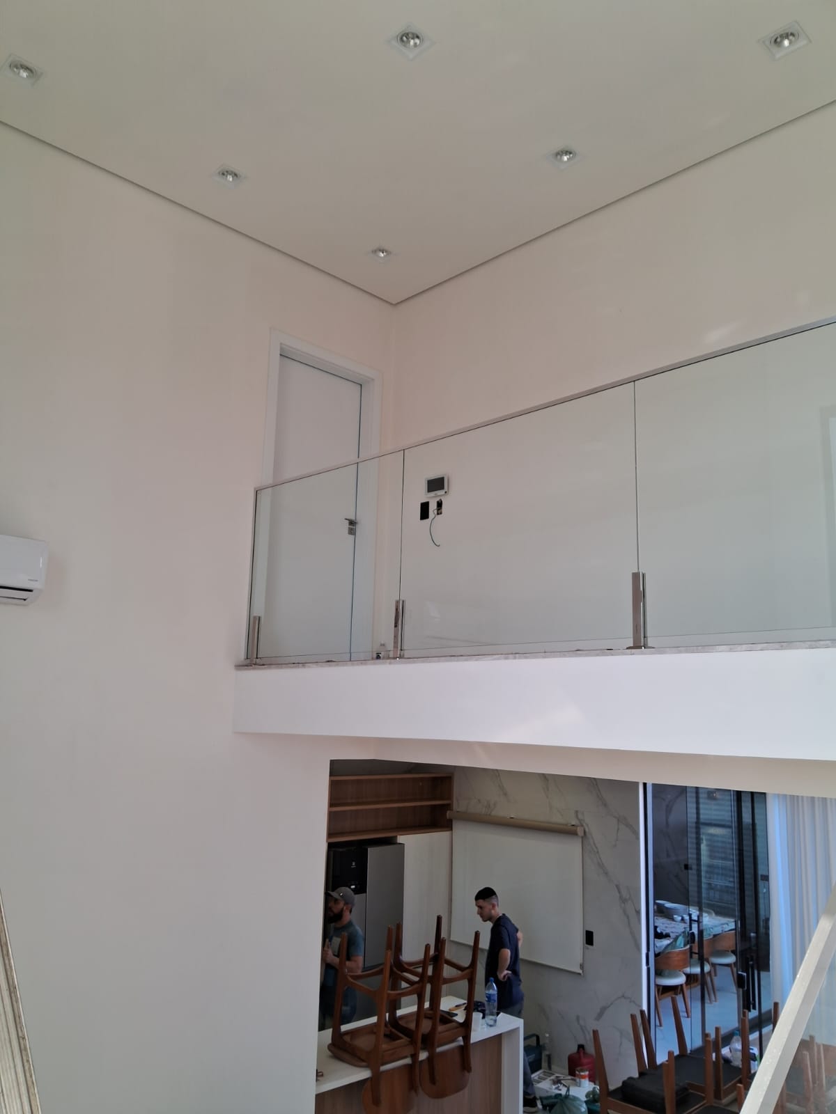 Sala com pé-direito duplo e paredes brancas recém-pintadas, com mezanino em vidro