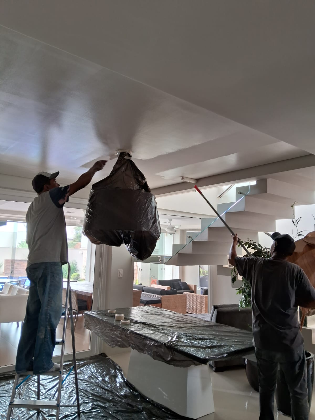 Equipe da JG Pinturas pintando o teto de uma sala com tudo protegido por lona